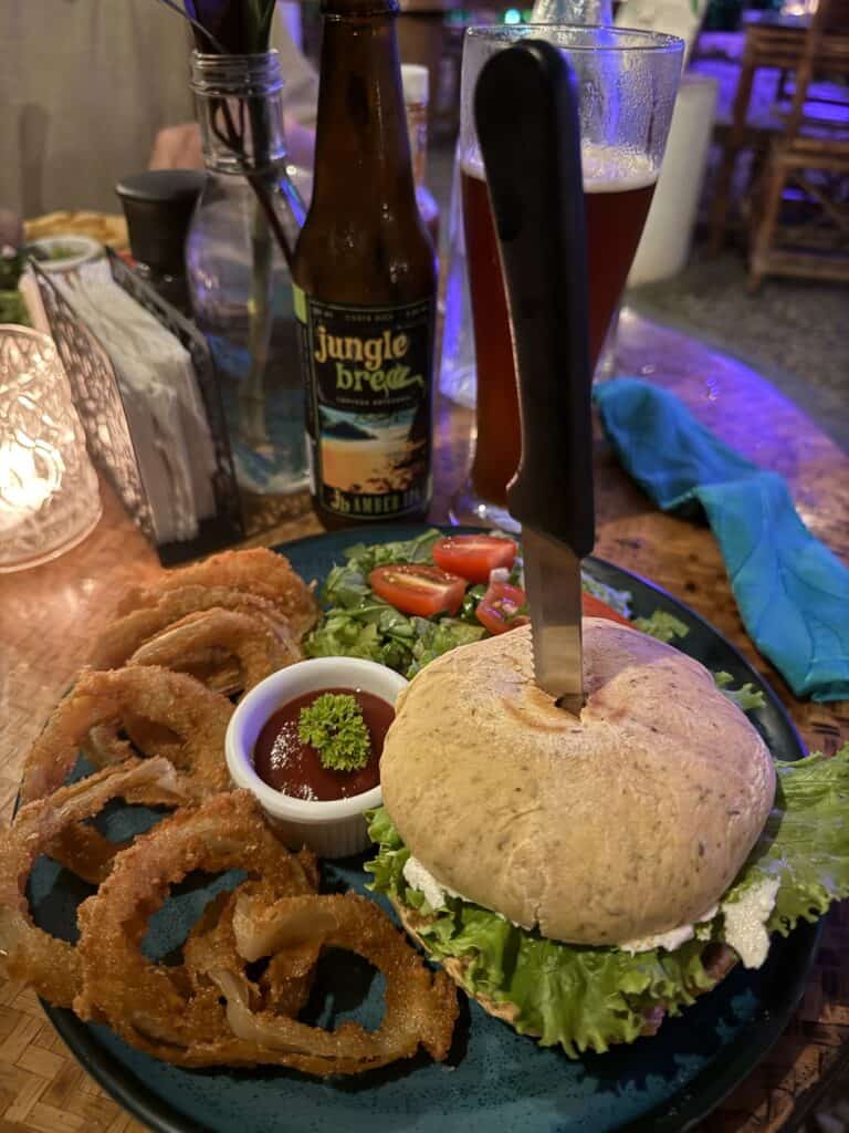 hamburger with knife in the top and side of onion rings. Food is from Indomitos Uvita Costa Rica.